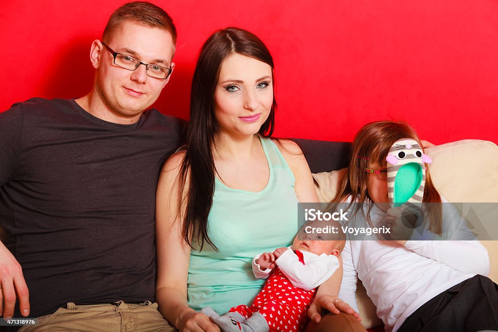 Family with newborn baby girl portrait Parenthood and happiness concept. Young family mother father and child preschooler sitting on sofa with newborn baby girl at home 2015 Stock Photo