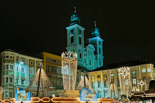 Linz, Austria- December 18, 2008: at the lighted Christmas market in Hauptplatz you can see different paintings on the top of each stalls. On the background is the imposing Jesuitenkirche or Alter Dom, the old Cathedral, built by the Jesuits in the years 1669-1683.