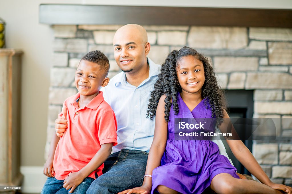 Father and Children A single father with his two children in his beautiful home with a fireplace in the background. 2015 Stock Photo