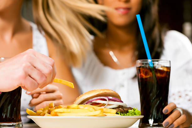 dos mujeres comiendo hamburguesas y bebidas gaseosas - white food and drink industry hamburger cheeseburger fotografías e imágenes de stock