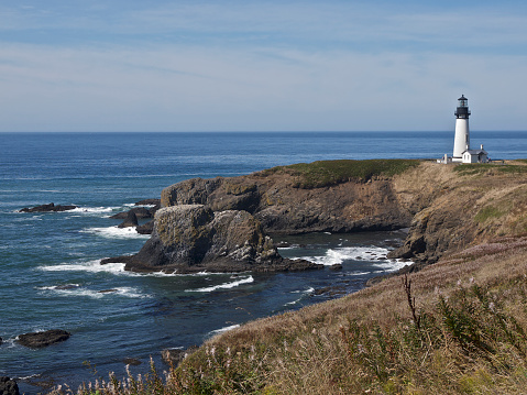 Yaquina Head Lighthouse on the Pacific Ocean in Oregon. This is near the town of Newport, Oregon. This is a historic area from the mid 1800's. The grassy cliff is part of Yaquina Head, a narrow headland that extends into the Ocean.