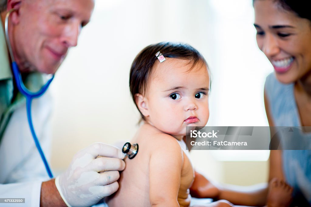 Baby at the Doctors Office A little baby girl in her diaper at the doctors office with her mother, the doctor is listening to the baby's heartbeat through a stethoscope while at the appointment. Looking At Camera Stock Photo