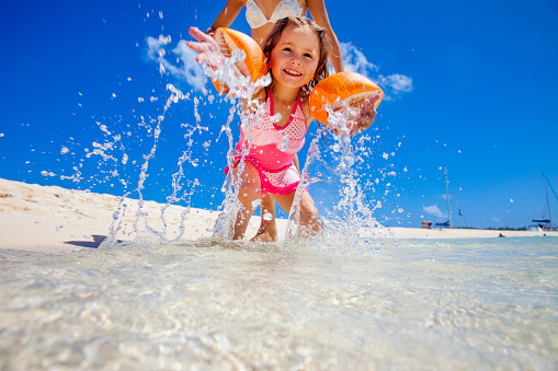 Little girl in shallow water on beach spraying water towards the camera