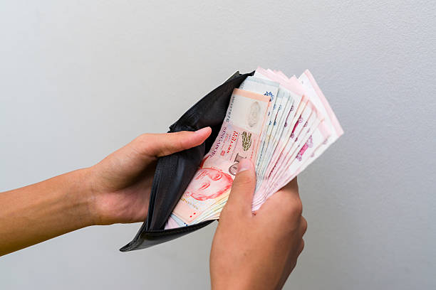 Wallet with money Close up of a pair of man hands holding a black leather wallet showing large sum of Singapore dollar note in it. singapore cash stock pictures, royalty-free photos & images