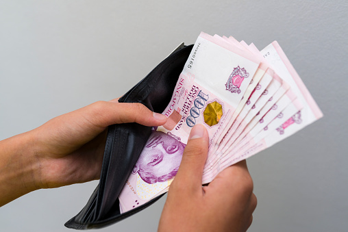 Close up of  a pair of man hands holding a black leather wallet showing large sum of Singapore dollar note in it.
