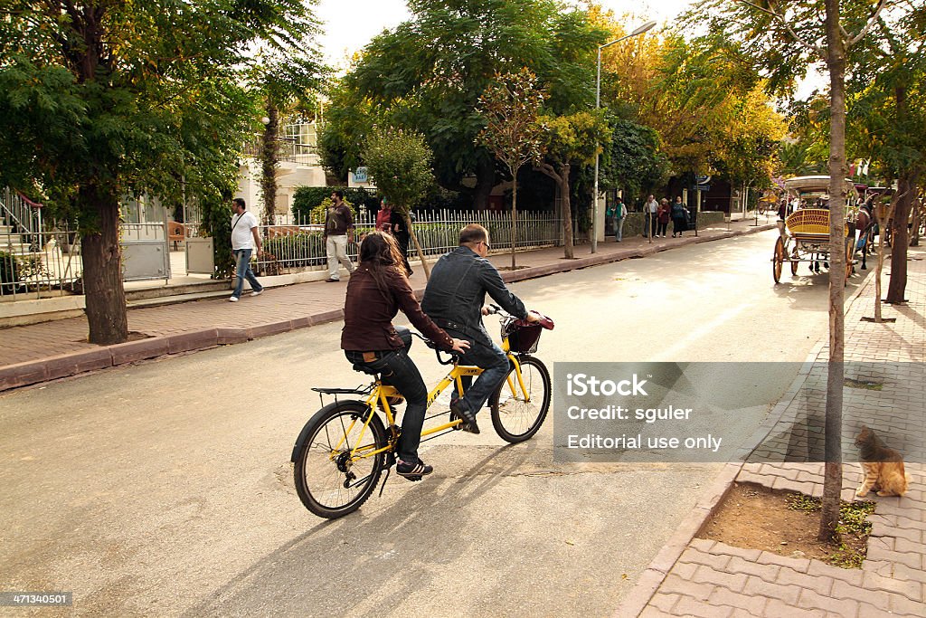 young couple riding tandem bicycle Istanbul,Turkey-October 01,2010:Young couple riding tandem bicycle on buyukada street, istanbul.Buyukada island is one of the princess islands near istanbul Turkey.Residents and tourists are not allowed to drive cars on the island.Carriages and bicycle are the main mode of transportation. Couple - Relationship Stock Photo