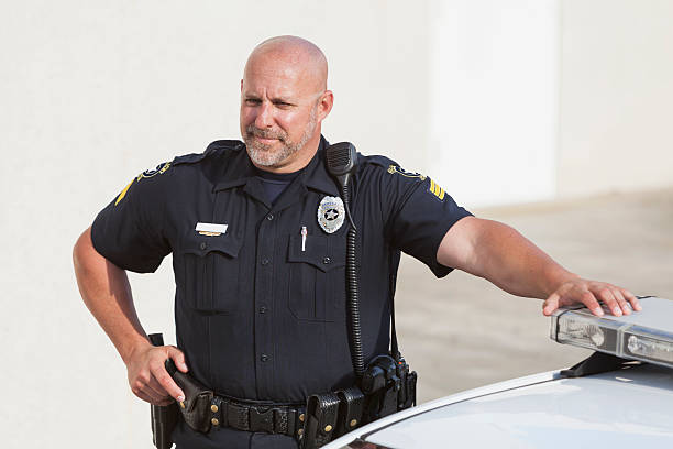 istock Serious police officer standing next to cruiser 471345106