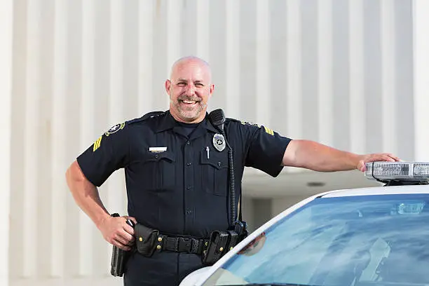 Photo of Happy police officer standing next to cruiser