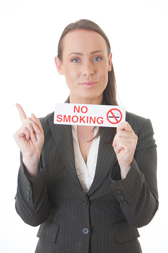 A business woman dressed in a business suit holds a no smoking sign. Isolated on white.