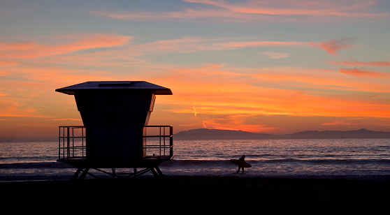 Beautiful sunset on Hollywood Beach with silhouette of a lifeguard stand and a lone surfer.   Near Oxnard, Ventura county, California. 