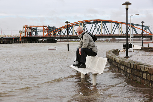 Active senior keeping his feet dry in the flooded street at the river bank of the city \