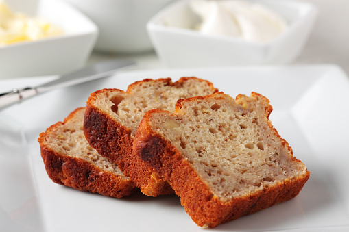 Banana Bread loaf on a plate with butter and cream cheese in the background.