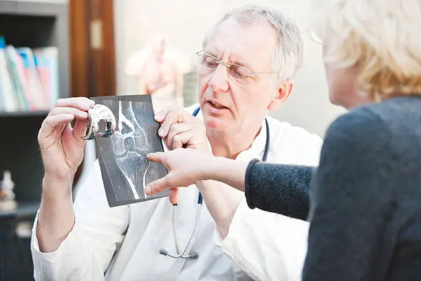 Photo of Mature doctor presenting x-ray and knee arthroplasty to female patient