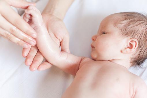 Mother makes massage for happy baby, apply oil on the hand, with white background