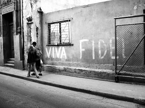 Havana, Cuba - January 11, 2006: Young couple is passing a wall in old Havana, with the words  
