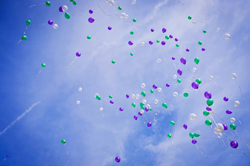 A huge group of colorful balloons flying up on a blue sky. Wide horizontal composition.