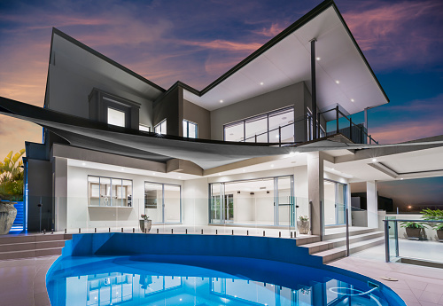 Modern new luxurious mansion exterior with swimming pool and reflections at dusk with pink and blue sky on the Gold Coast, Queensland, Australia