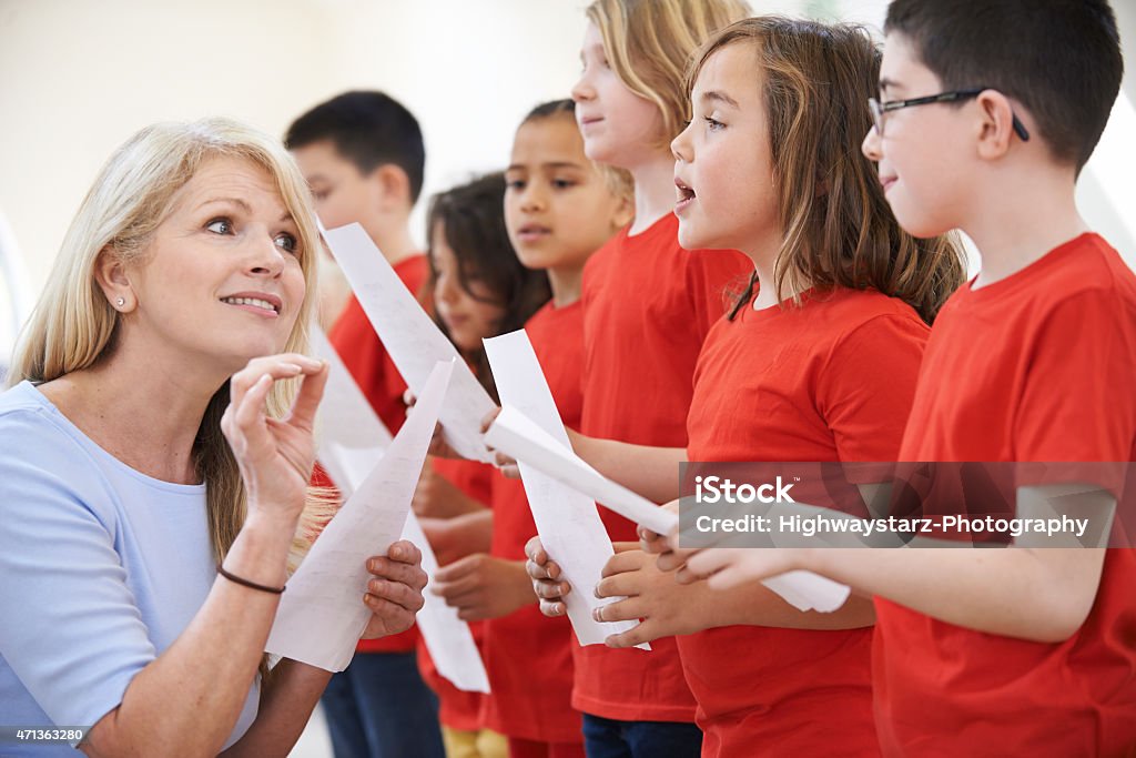 Teacher instructs a children's choir dressed in red Children In Singing Group Being Encouraged By Teacher Choir Stock Photo