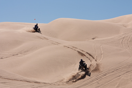 Two ATVs wind their way, racing up the hilly Dunes in California's Imperial Sand Dunes.