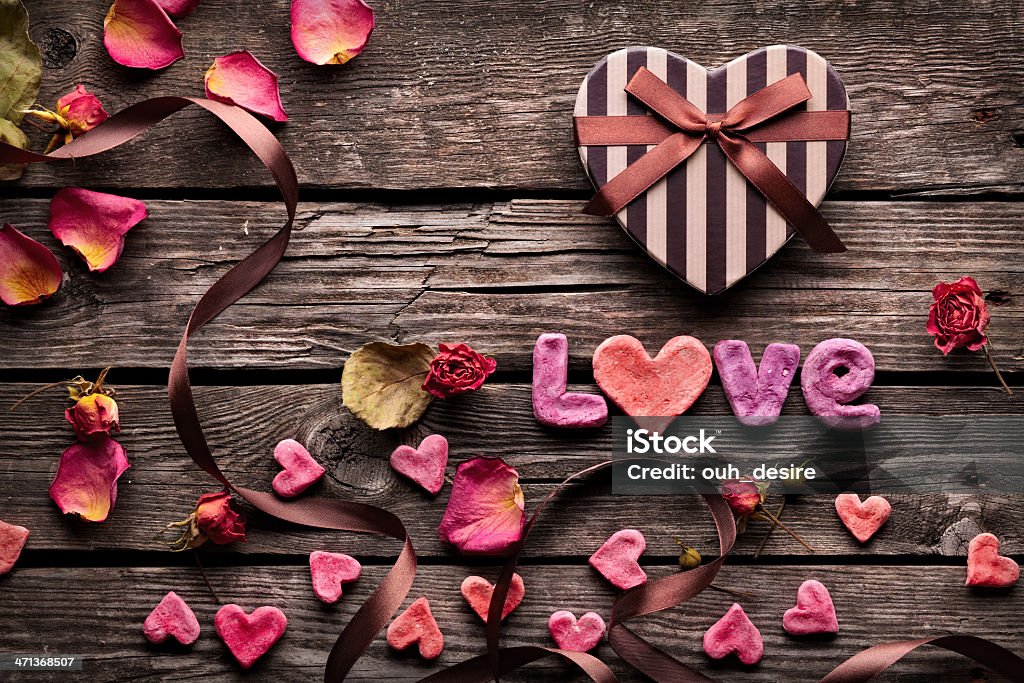 Word Love on wooden plates. Word "love" is laid out with nice letters. Lovely Valentines Day background with many rose petals, rose flowers and cute small hearts. Abstract Stock Photo