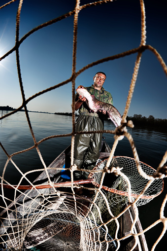 Fisherman holding a catfish behind a fishing net.