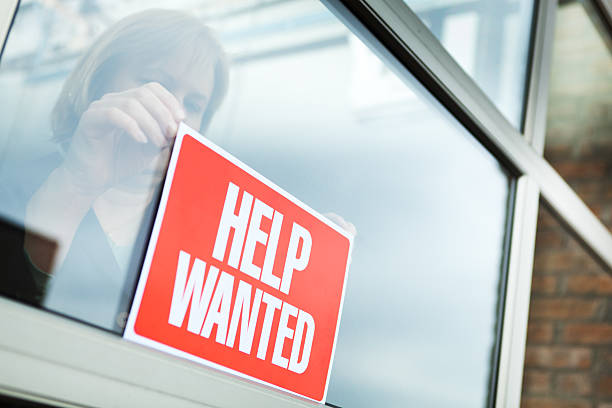 HELP WANTED Recruitment Sign Displayed for Hiring, Employment, Economic Recovery Sign of hiring, recruitment, employment and economic recovery through a woman business person posting a "HELP WANTED" sign for new employees. help wanted sign photos stock pictures, royalty-free photos & images