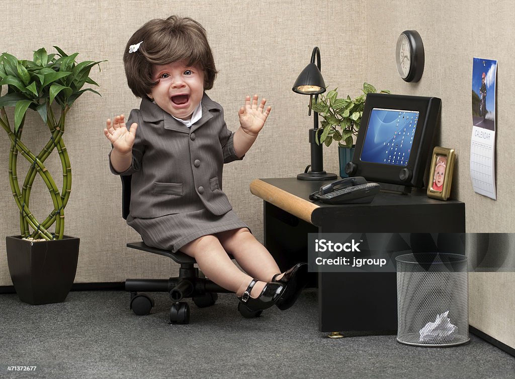 Career Crisis Baby sitting in a business cubicle wearing a business dress with an expression of panic on her face Humor Stock Photo