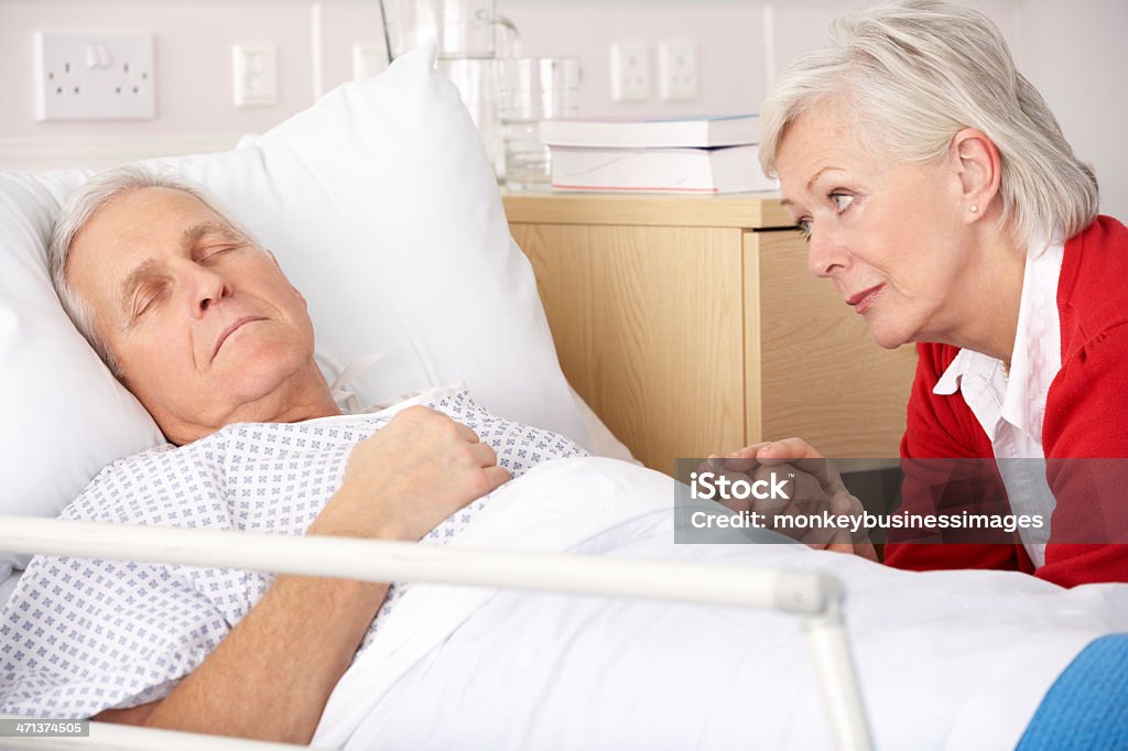 Senior woman visiting husband in hospital Senior woman visiting husband in hospital ward, holding his hand while he is sleeping 60-69 Years Stock Photo