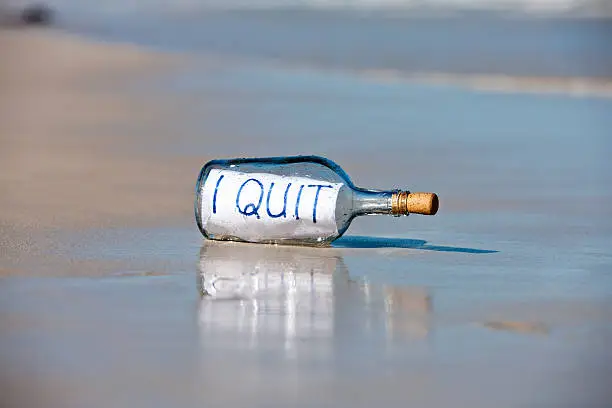A bottle containing a message saying "I quit" is washed up on the sand at the water's edge. This castaway has evidently had enough or possibly given up a bad habit! 