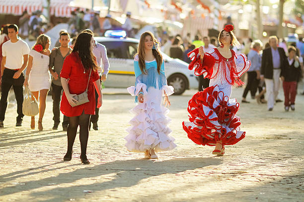 Seville, Spain - May 7, 2011: There is something for everyone during the fair, also for adolescents, 3 girls, 2 od them with  with multicolor flamenco dresses walks around the fairground of the Seville event talking, laughing and even pulling and impromptu dance step.