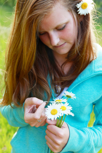 A portrait of a teen girl picking at the petals of a daisy, playing 