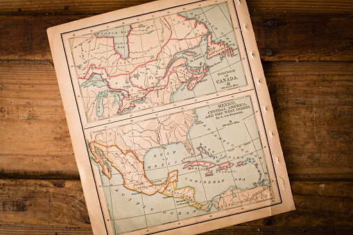 Color image of  old color maps of Canada and of Mexico, Central America, and the West Indies, sitting at an angle, on antique wood trunk.