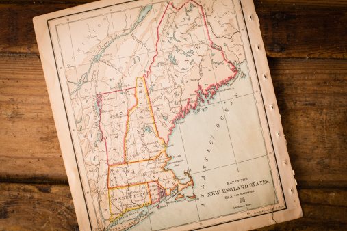 Color image of an old map of the New England States, sitting at an angle on antique wood trunk.