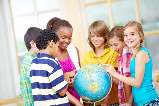 Happy group of young children pointing at countries on a world globe - portrait