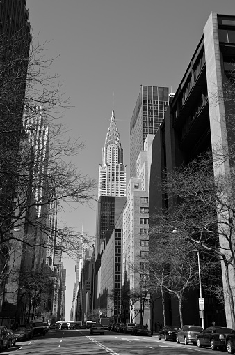 A cityscape view of 20th century architectural styles of corporate skyscrapers seen along East 42nd Street in Midtown Manhattan, New York City. The iconic Art Deco Style Chrysler Building is seen towering over neighboring buildings in midday sunlight.