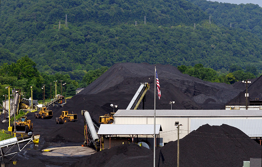 Mounds of coal are piled high awaiting shipment at a coal company terminal in West Virginia, USA. Part of the Appalachian Mountains are seen in the background.