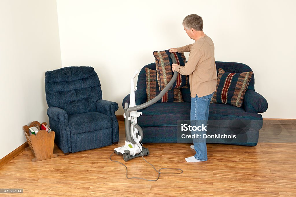 Uomo aspirapolvere un divano cuscino - Foto stock royalty-free di Addetto alle pulizie