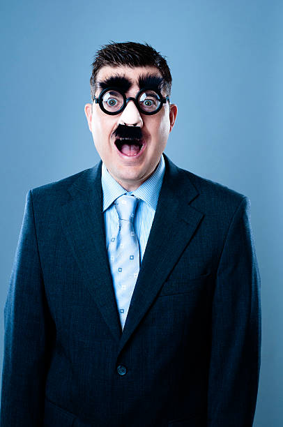 Funny looking and crossed eyed businessman is disguised by a plastic nose, fake mustache and eyebrows. He is also wearing glasses and looks really surprised. 