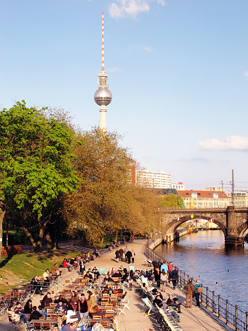 Berlin, Germany - April 25, 2012: Big group of people sitting in a typical Berlin beer garden at Spree River located at Cental Berlin  (Germany). In background the television tower.