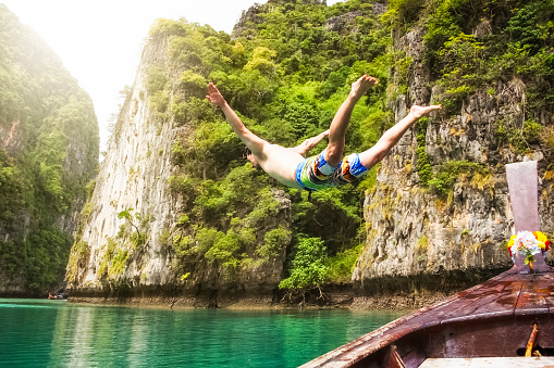 young man jumps from a boat in Maya Bay - Koh Phi Phi Leh / Thailand. 