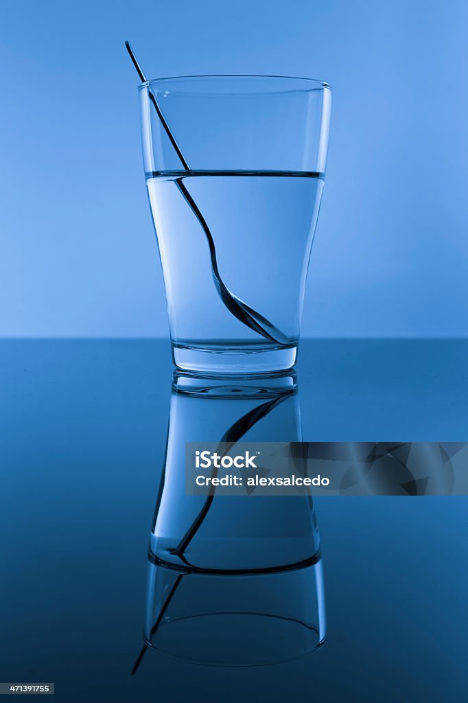 Blue glass Glass of water with spoon in blue background with reflection. Refraction Stock Photo