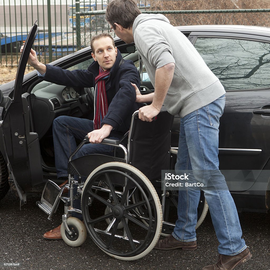 Man Helping a Disabled person A man helping a disabled man to get down from car on his wheelchair. Square shot. Wheelchair Stock Photo