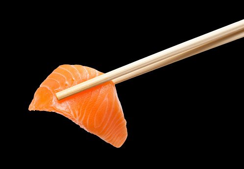 Sliced raw salmon with chopsticks holding it, isolated on black
