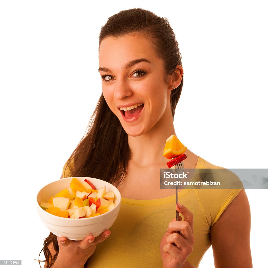 Caucasian woman holding white bowl of choped fruit and fork Beautiful happy asian caucasian woman in yellow t-shirt holding white bowl of fruit choped on pieses and eating it with fork. Healthy lifestyle concept isolated over white. 2015 Stock Photo