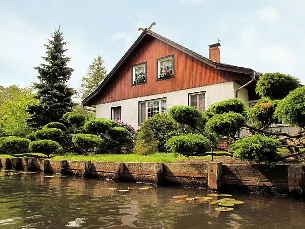 One of this typical houses along the canal at Spreewald (Brandenburg, Germany) near by village Luebbenau. In front some coniferous tree. In top of house a carving of traditional snake god, going back to sorbs religion. The Spreewald (German for "Spree forest") is located around 100 km south-east of Berlin. A biosphere reserve by UNESCO since 1991. traditional irrigation system with of more than 200 small canals. tourist manget of Brandenburg.