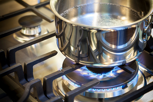 Gas burner on stove with flame on stainless steel surface showing heat ready for cooking food. Stainless steal pot on burner cooking food.