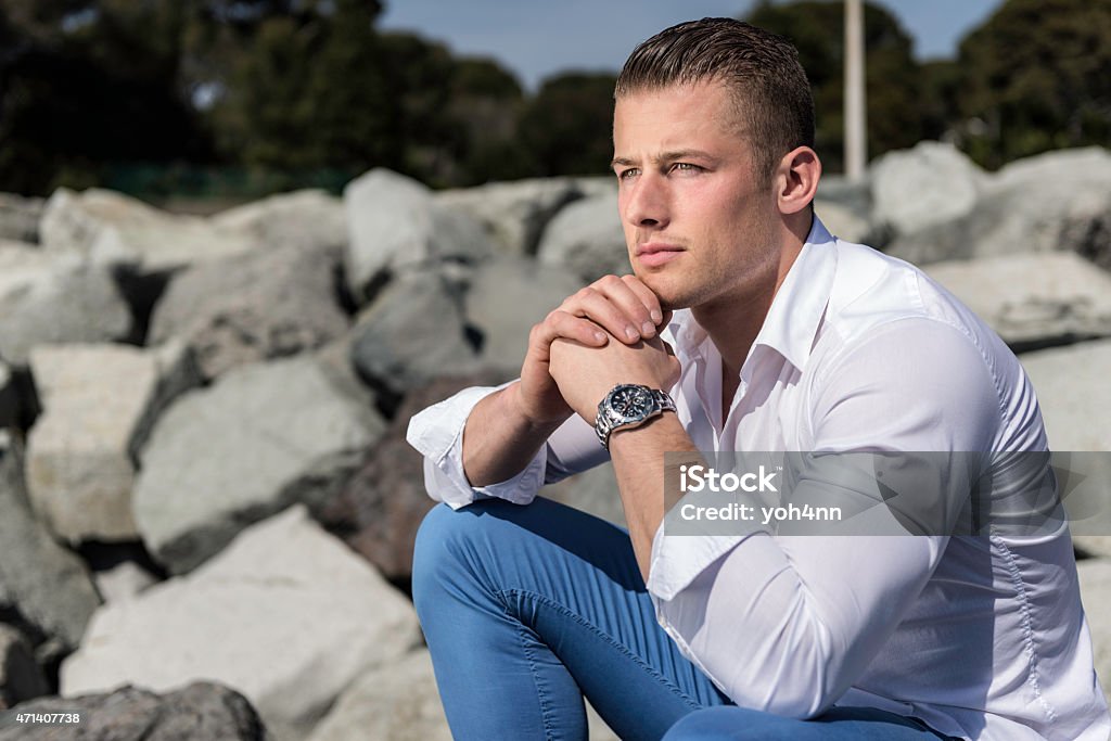 Confident man sitting and thinking Confident man sitting. He is pose, relax and looks at the beautiful sunset, enjoy the holidays. He has blond hair, blue eyes and wear blue trousers with white shirt. 20-24 Years Stock Photo