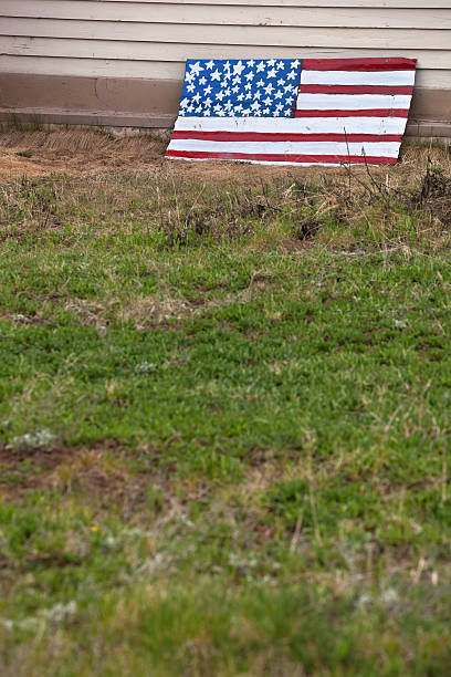 handmade backyard americana abandoned home green grass backyard with american flag painted and leaning on wall conjures notions of the american dream. vertical composition taken in silverton, colorado. colorado flag art pictures stock pictures, royalty-free photos & images
