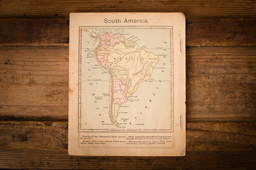 Color image of an old color map of South America, from the 1800's, sitting on wood background.