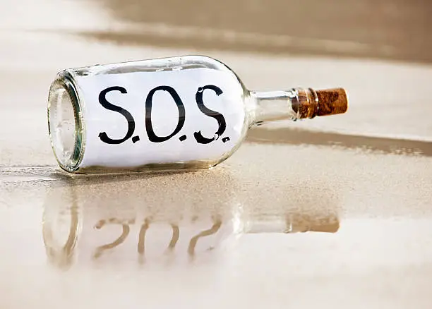 A bottle containing a desperate  message saying "SOS", presumably from a frantic castaway, is washed up on the shore and reflected in the sand. 